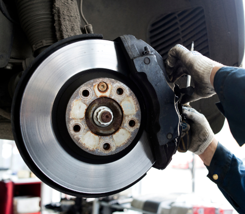 An image of a technician changing brakes on a car in an automotive service bay. 