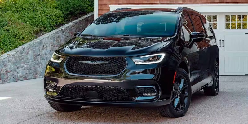 An image of a black 2024 Chrysler Pacifica sitting in a driveway in front of the garage. 