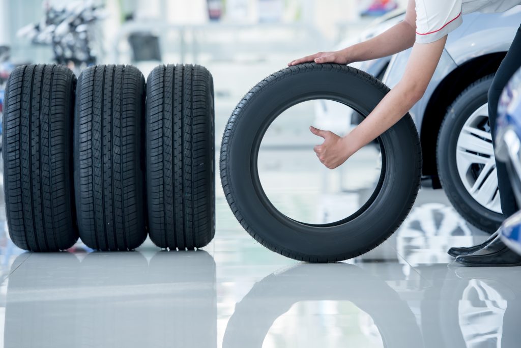 An image of four tires on a service room floor. One tire is sideways, being held by a technician who is given a thumbs up. 