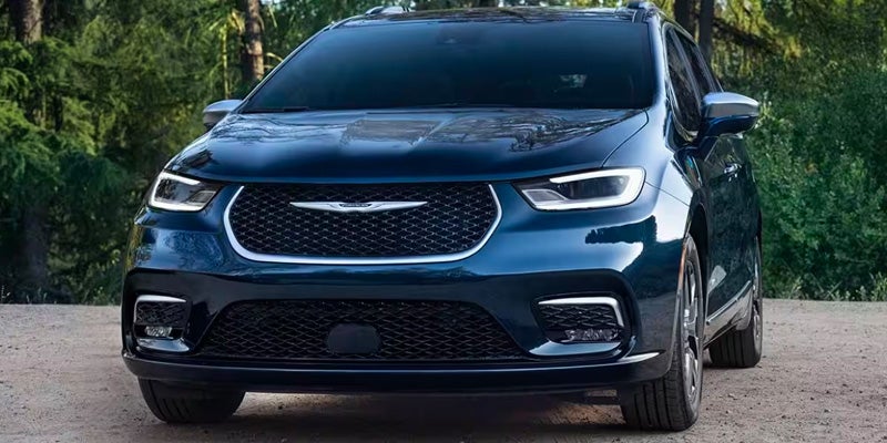 A black Chrysler Pacifica PHEV sitting against a forested backdrop. 