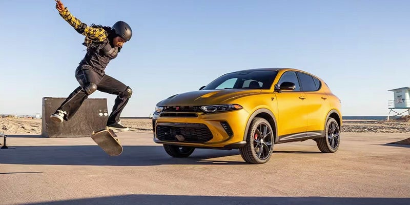 A skateboarder performing an "ollie" in front of a gold 2024 Dodge Hornet on a parking pad.