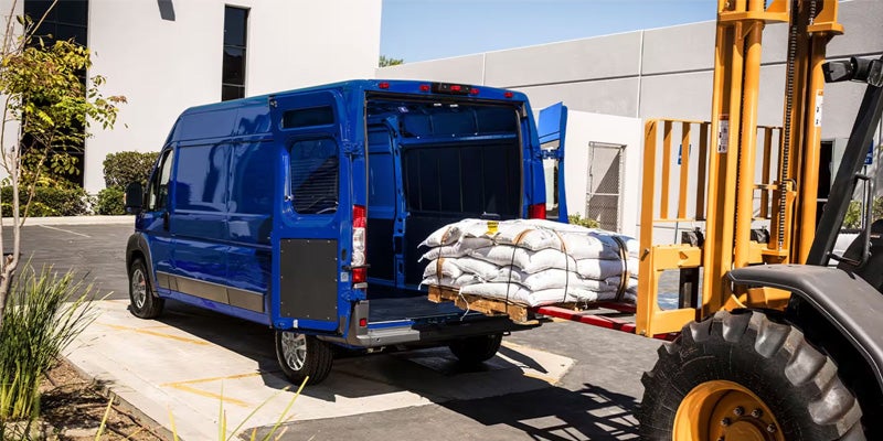 A blue 2024 RAM ProMaster being loaded with heavy cargo with the use of a cargo lifter, showcasing its powerful cargo capacity. 
