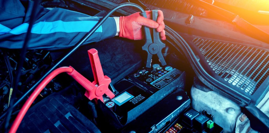Under the hood of a Jeep, a person is holding a clamping a charging cable to the battery terminal in Shiloh, IL