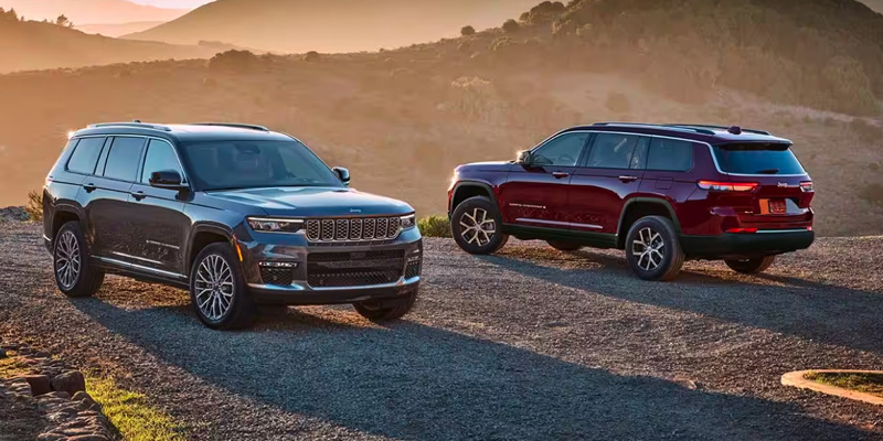 Dual Jeep Grand Cherokees sitting, facing opposite directions, in a desert landscape as the sun sets behind them. One SUV is red, the other black.