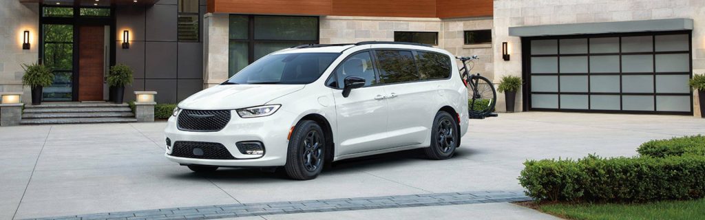 a white Chrysler Pacifica PHEV minivan is parked in a driveway in front of a modern house in Shiloh, IL