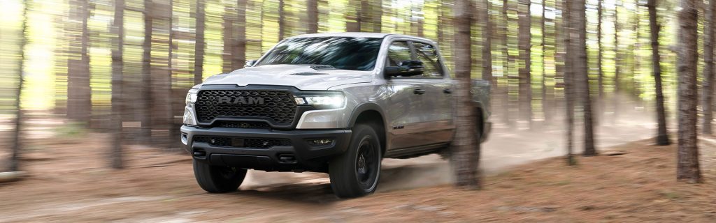 Silver RAM truck driving through forest trail.