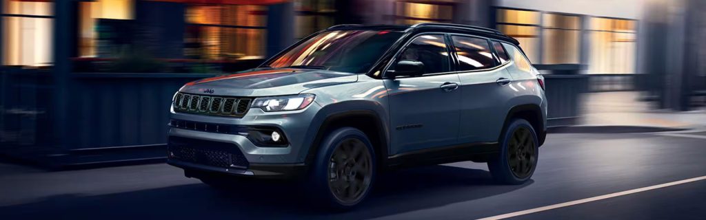 Silver Jeep Compass SUV driving on a city street, showcasing its sleek design and sporty urban style.