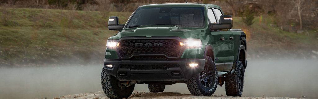 Green RAM Rebel pickup truck driving off-road through misty terrain.