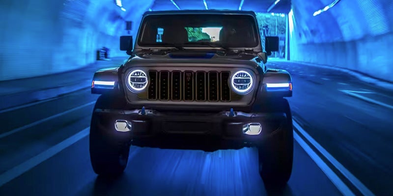 A Jeep Wrangler, head-on, with its LED headlights illuminated